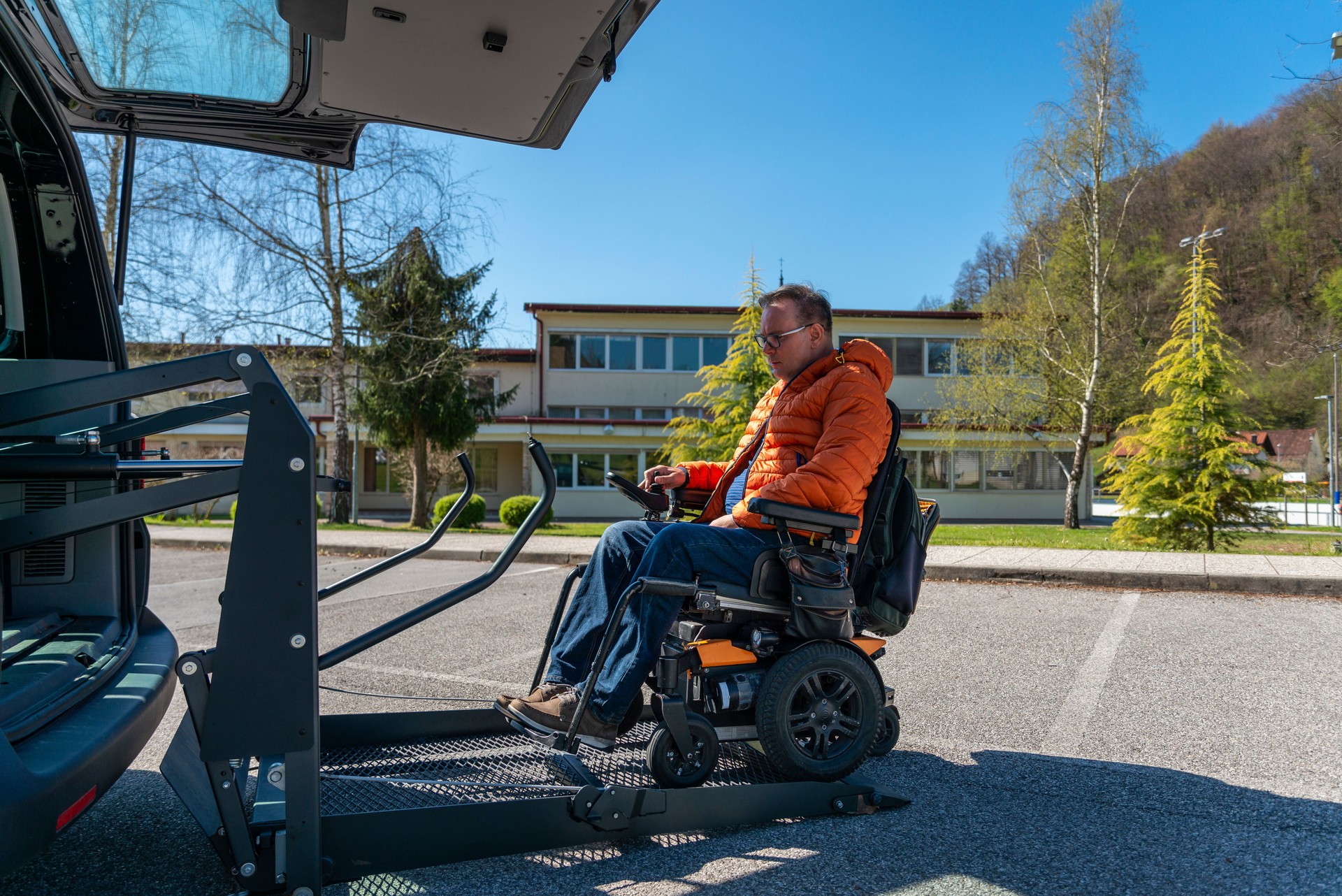 Disabled man in a motorized wheelchair when entering a van on an electric lift. In front of the vehicle, on the vehicle.